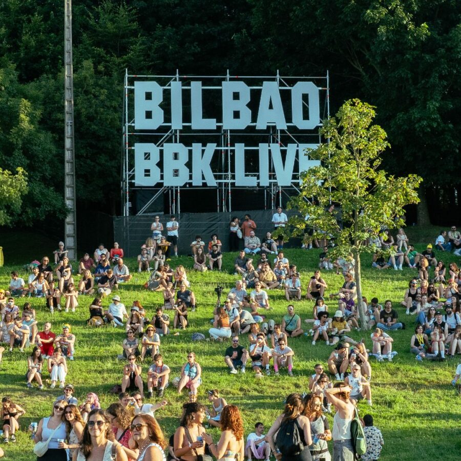 Gente descansando el la campa de Bilbao BBK Live 2025 con el logo del festival de fondo